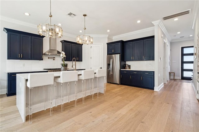 kitchen featuring stainless steel fridge, light wood-style flooring, wall chimney exhaust hood, and visible vents