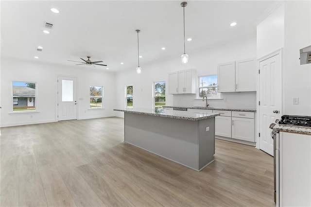 kitchen with light stone countertops, a kitchen island, light wood-style flooring, and white cabinets