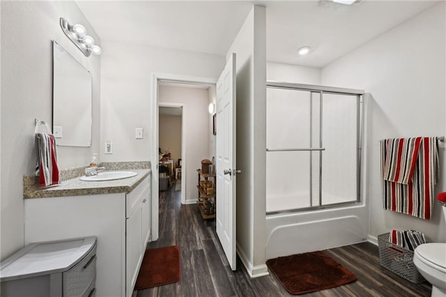 full bathroom with toilet, wood finished floors, combined bath / shower with glass door, baseboards, and vanity