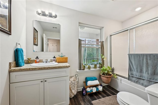 bathroom featuring vanity, toilet, wood finished floors, and enclosed tub / shower combo