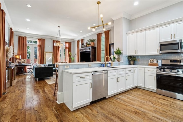 kitchen featuring open floor plan, appliances with stainless steel finishes, a peninsula, an inviting chandelier, and a sink