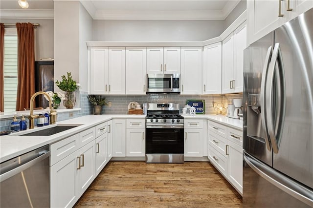 kitchen with light wood finished floors, a sink, stainless steel appliances, light countertops, and crown molding