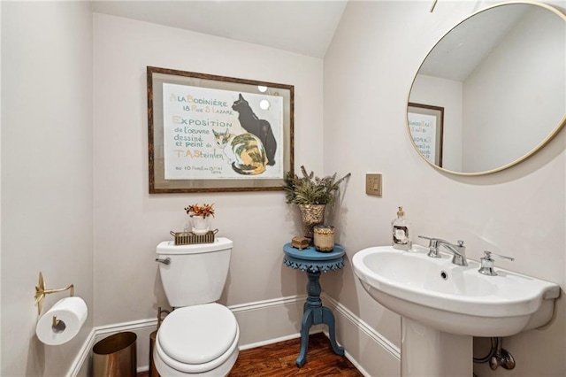 half bath with toilet, wood finished floors, baseboards, and a sink