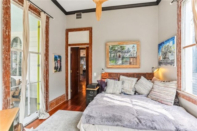 bedroom featuring visible vents, baseboards, wood finished floors, and ornamental molding