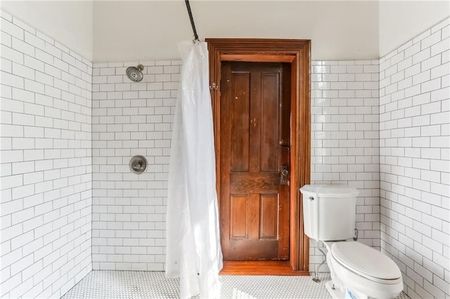 full bathroom with tile patterned flooring, tile walls, toilet, and tiled shower