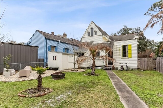 rear view of house with a fenced backyard, an outdoor fire pit, an outbuilding, and a yard