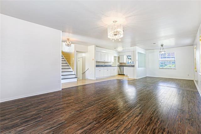 unfurnished living room featuring stairway, a notable chandelier, light wood-style floors, and baseboards