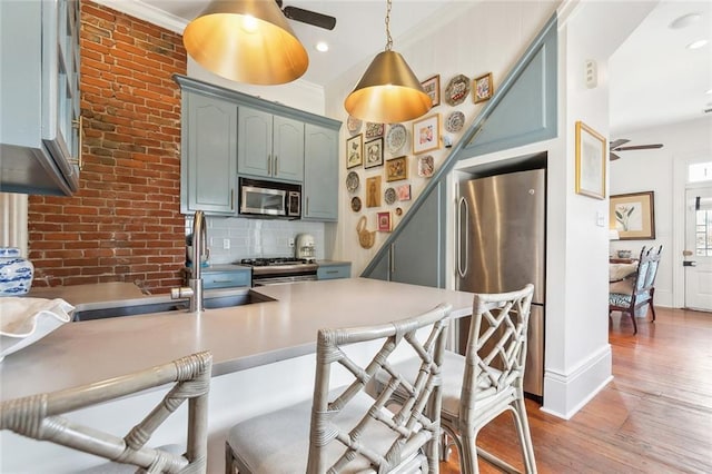 kitchen with a breakfast bar, ornamental molding, backsplash, stainless steel appliances, and light wood finished floors