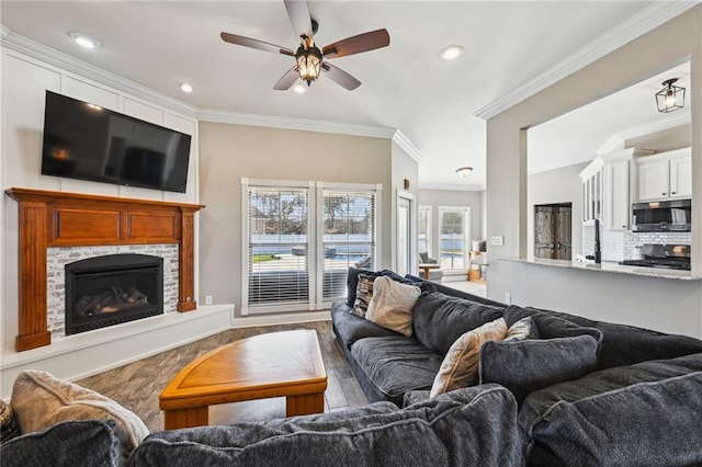 living area with wood finished floors, a fireplace with raised hearth, recessed lighting, ceiling fan, and crown molding