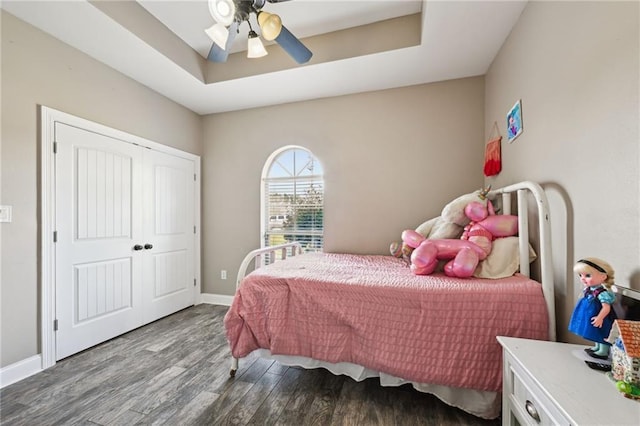 bedroom featuring baseboards, a raised ceiling, a closet, and wood finished floors