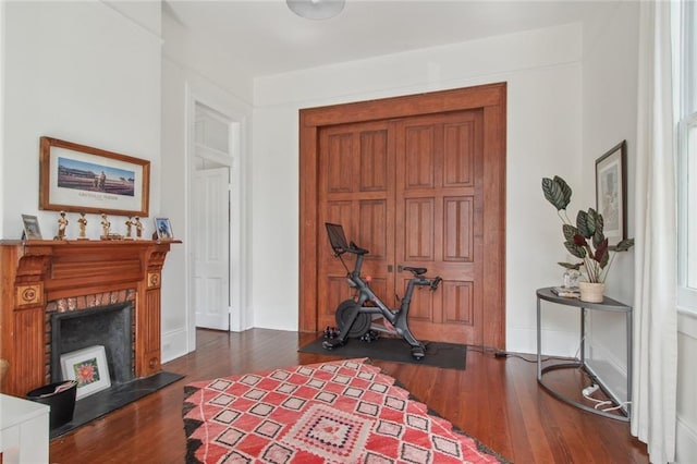 exercise area featuring baseboards, a lit fireplace, and wood finished floors