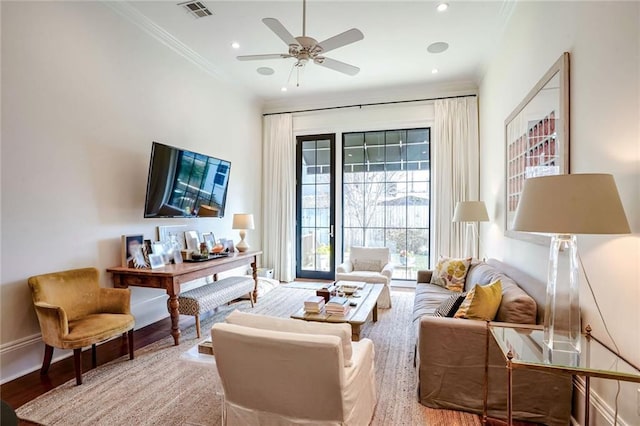 living area with visible vents, ornamental molding, a ceiling fan, wood finished floors, and baseboards