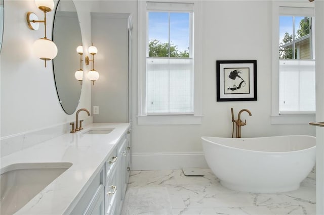 full bath featuring plenty of natural light, marble finish floor, a freestanding tub, and a sink