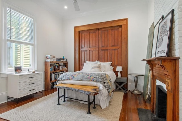 bedroom featuring wood finished floors, baseboards, a fireplace with flush hearth, ceiling fan, and crown molding