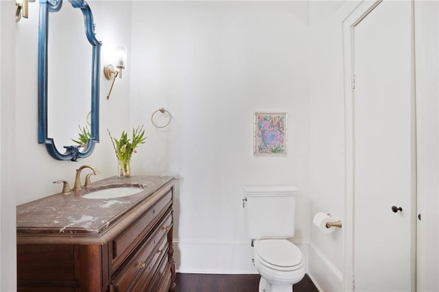 half bath with toilet, vanity, and wood finished floors