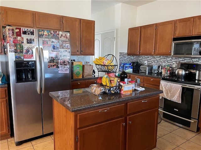 kitchen with dark stone countertops, tasteful backsplash, a center island, stainless steel appliances, and light tile patterned flooring