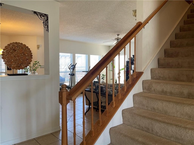 stairway featuring tile patterned floors, a ceiling fan, baseboards, and a textured ceiling