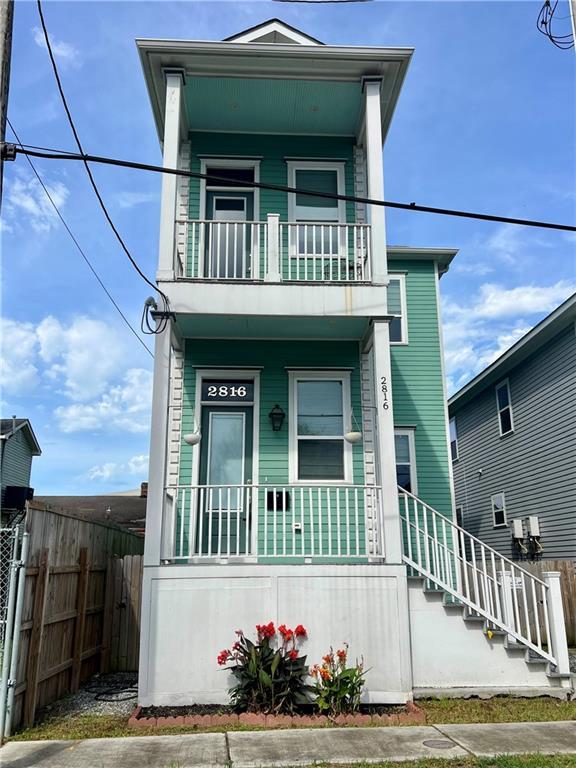view of front facade featuring fence, a balcony, stairway, and covered porch