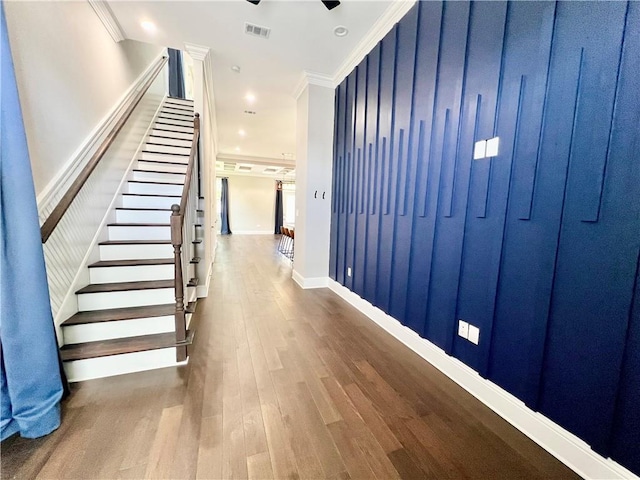 hall featuring visible vents, crown molding, wood finished floors, baseboards, and stairs