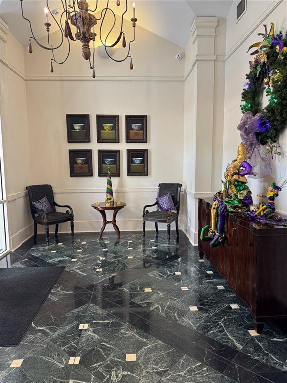 living area featuring decorative columns, visible vents, marble finish floor, and a chandelier