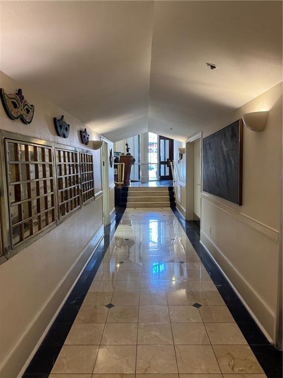 hall featuring tile patterned floors, mail area, baseboards, and vaulted ceiling