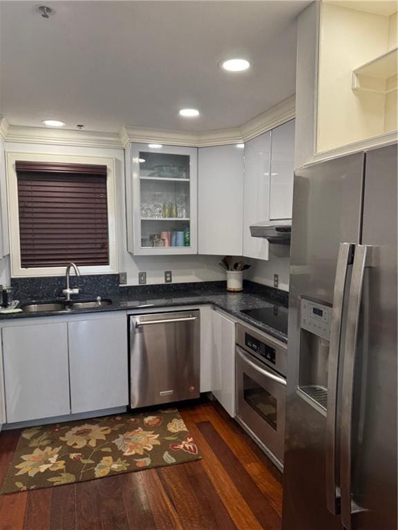 kitchen featuring a sink, dark wood-type flooring, glass insert cabinets, under cabinet range hood, and appliances with stainless steel finishes