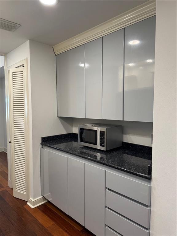 kitchen featuring dark stone countertops, stainless steel microwave, visible vents, and dark wood-style flooring