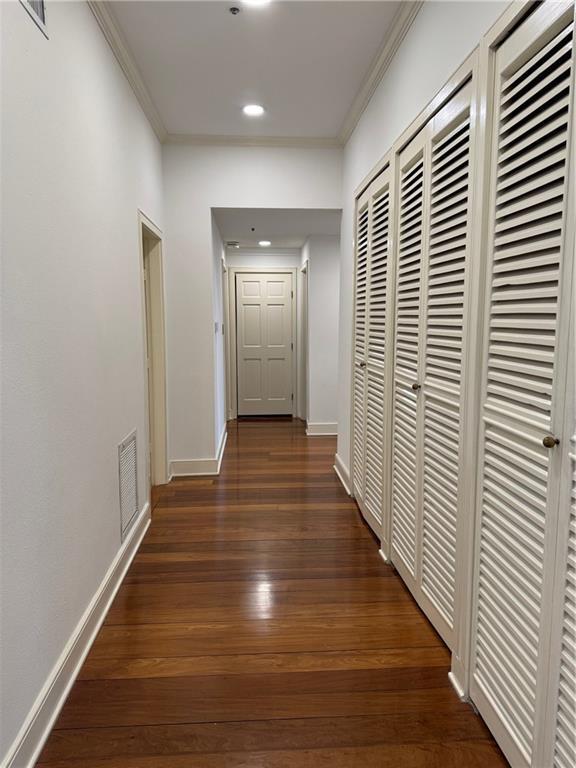 corridor with dark wood-style floors, visible vents, baseboards, recessed lighting, and crown molding