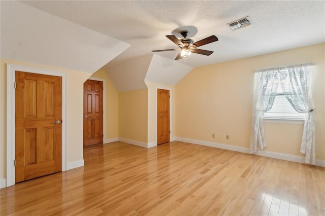 additional living space with a ceiling fan, visible vents, lofted ceiling, light wood-style flooring, and a textured ceiling