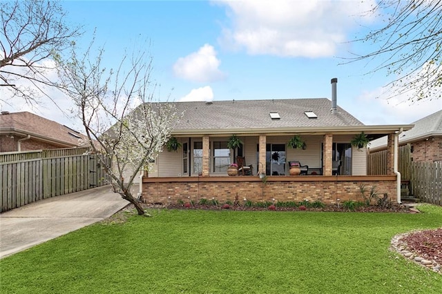 view of front of home with a porch, fence, roof with shingles, a front yard, and brick siding