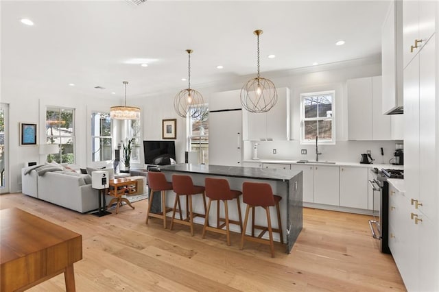 kitchen featuring a kitchen island, a sink, white cabinets, stainless steel gas range oven, and light wood-type flooring