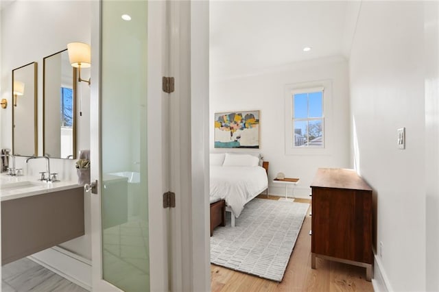 bedroom with ornamental molding, baseboards, light wood finished floors, and a sink