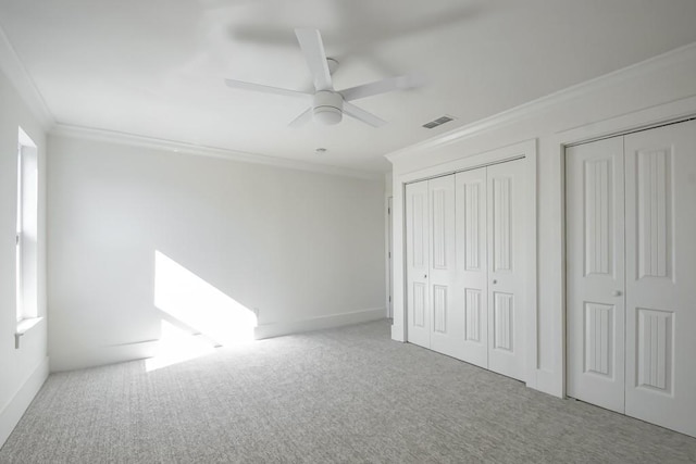 unfurnished bedroom with visible vents, two closets, ornamental molding, a ceiling fan, and carpet floors