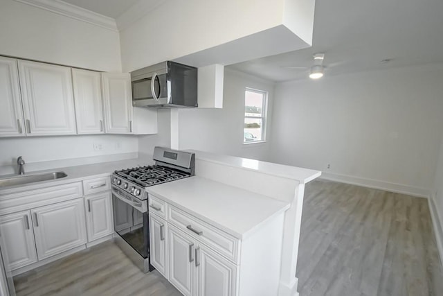 kitchen featuring light wood finished floors, a peninsula, a sink, appliances with stainless steel finishes, and white cabinetry