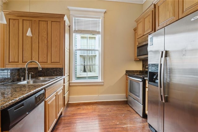 kitchen featuring a sink, baseboards, appliances with stainless steel finishes, brown cabinetry, and wood-type flooring