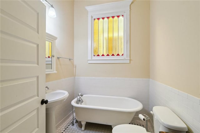 bathroom with tile walls, a freestanding tub, toilet, and wainscoting