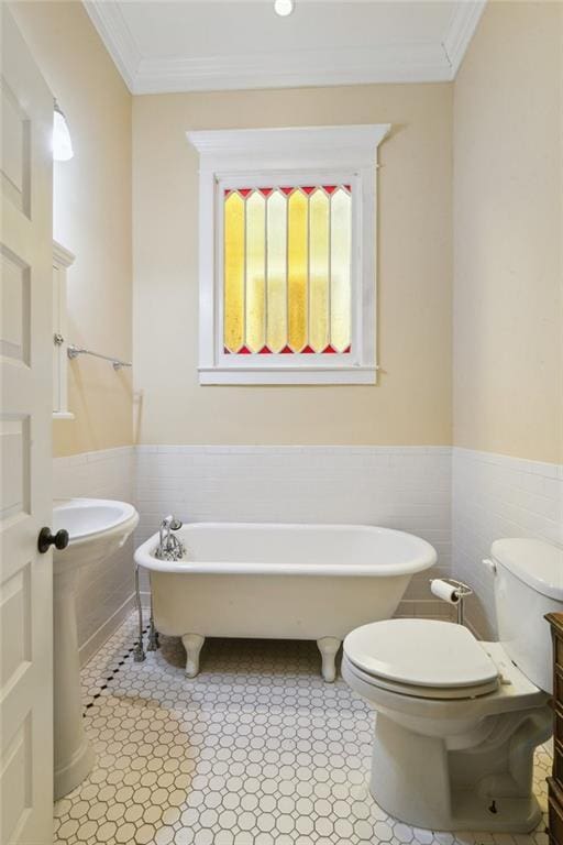 bathroom featuring crown molding, a freestanding bath, toilet, wainscoting, and tile walls