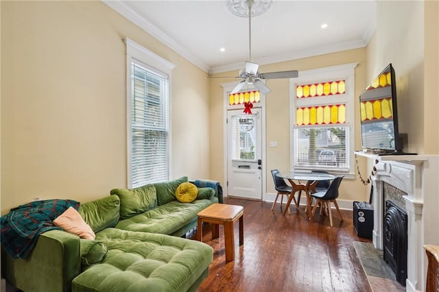 living area featuring a fireplace with flush hearth, ornamental molding, wood finished floors, baseboards, and ceiling fan