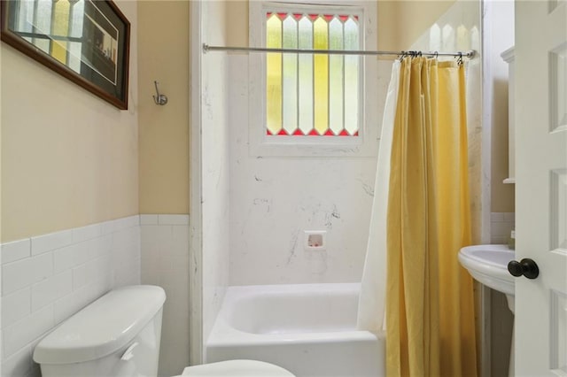 bathroom with a wainscoted wall, shower / bath combo with shower curtain, toilet, and tile walls