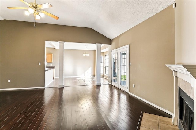 unfurnished living room featuring dark wood-style floors, ornate columns, lofted ceiling, a fireplace with flush hearth, and ceiling fan with notable chandelier