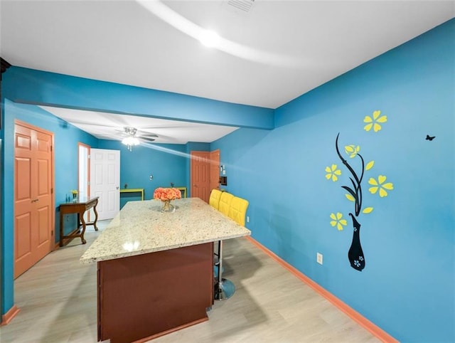 kitchen with light stone counters, baseboards, a kitchen island, a kitchen bar, and light wood-type flooring