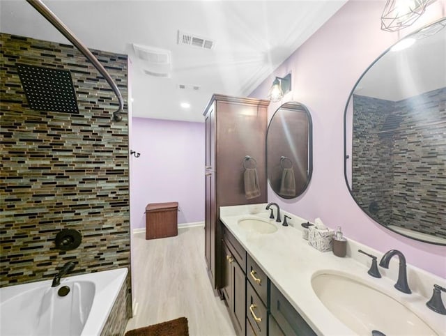 bathroom with wood finished floors, a tub to relax in, visible vents, and a sink