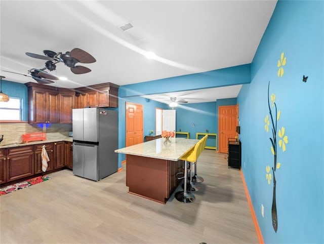 kitchen featuring backsplash, light stone countertops, a breakfast bar area, freestanding refrigerator, and light wood-style floors