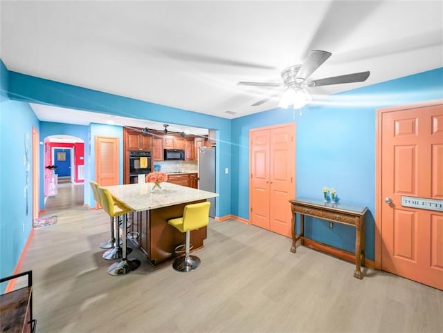 kitchen with light wood-style flooring, freestanding refrigerator, black microwave, a kitchen bar, and a center island