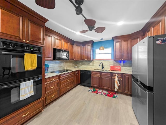 kitchen featuring light wood finished floors, tasteful backsplash, light stone countertops, black appliances, and a sink