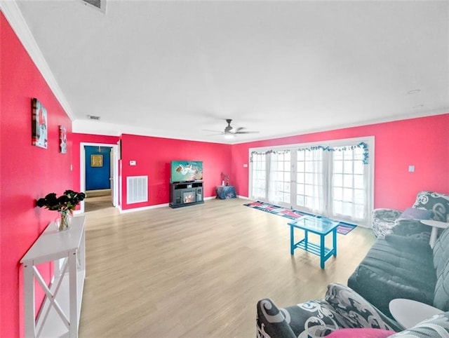 living room featuring a ceiling fan, wood finished floors, visible vents, baseboards, and crown molding