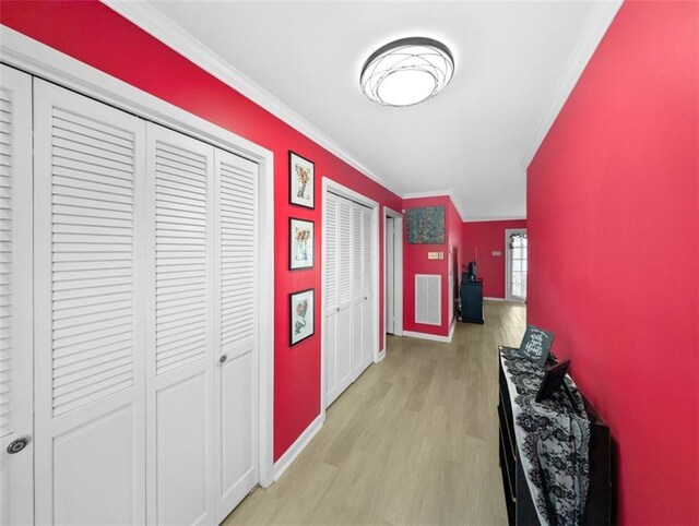 hall featuring visible vents, light wood-style flooring, crown molding, and baseboards