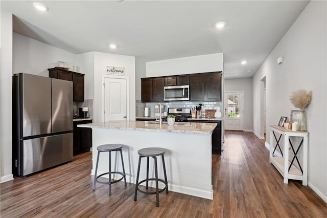 kitchen featuring stainless steel appliances, dark wood-style floors, a center island with sink, and decorative backsplash