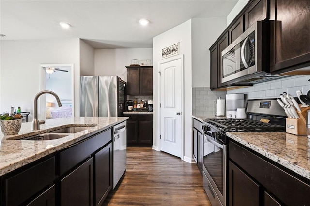 kitchen with tasteful backsplash, light stone countertops, appliances with stainless steel finishes, dark wood-style floors, and a sink