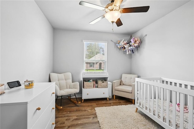 bedroom featuring a ceiling fan, a nursery area, and dark wood-style flooring